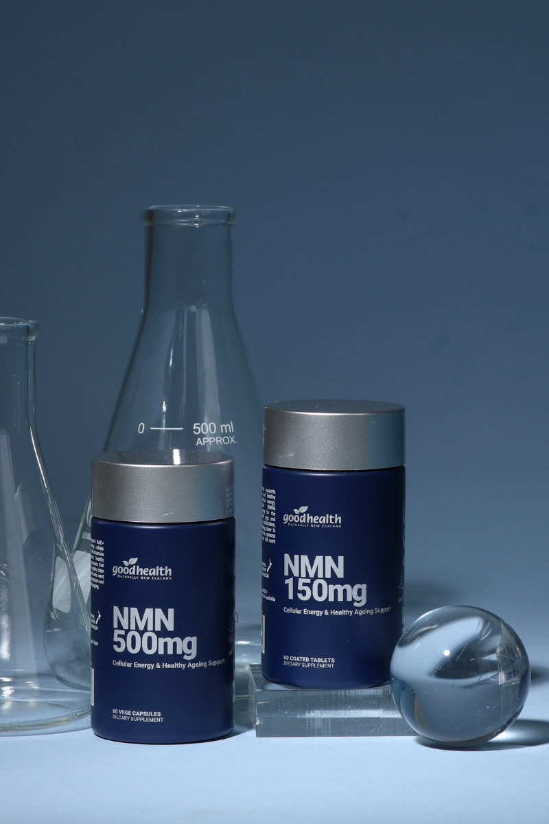 Two dark blue supplement bottles with silver caps labeled 'goodhealth NMN 500mg' and 'NMN 150mg', styled with glass laboratory equipment on a blue background.
