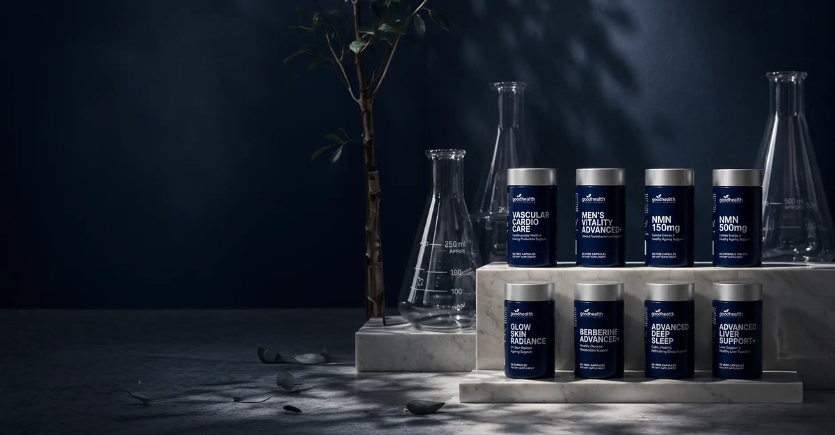 A set of dark blue supplement jars with silver lids arranged on white pedestals alongside clear glass flasks against a dark studio background with dramatic lighting.