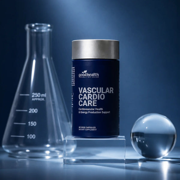 A dark blue supplement bottle labeled 'goodhealth VASCULAR CARDIO CARE' stands on clear acrylic blocks, with a glass beaker on the left and a glass sphere on the right, against a blue studio background.